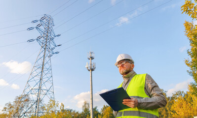 Male engineer maintains a telecommunications tower and power lines. Inspecting 4G and 5G network equipment. Control and maintenance of electrical installations for cellular communications.