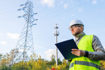 Male engineer maintains a telecommunications tower and power lines. Inspecting 4G and 5G network equipment. Control and maintenance of electrical installations for cellular communications.