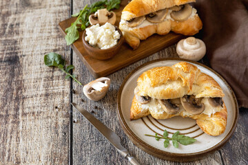 Freshly baked croissants with mushrooms and ricotta on rustic wooden table setting. Copy space.
