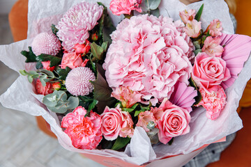 Feminine pastel pink bouquet featuring a large hydrangea, roses, mums, and alstroemeria, finished with a decorative pink pleated fan and white wrapping paper