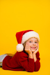 Funny cheerful kid in red knitwear and santa hat enjoys a sunny christmas moment on a bright yellow background