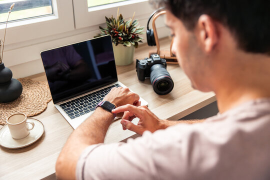 Young latin man teleworking and checking smartwatch at home