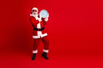 Santa Claus holds a clock wearing sunglass on a red background and promotes holiday cheer in a lively atmosphere