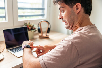 Young man teleworking getting surprised checking time on smartwatch