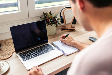 Young Hispanic man teleworking from home, studying, writing