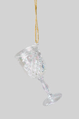 Minimal creative aesthetic view of Glass of wine Christmas ornament hanging on grey. New Year bright iridescent color glass toy as wineglass. Minimal concept of celebration, party and winter holiday.