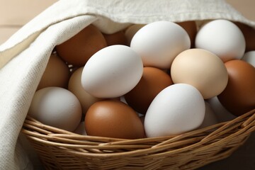 Many raw chicken eggs in wicker basket on table, closeup
