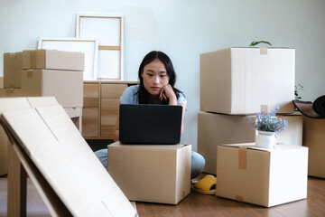 Female Asian use on laptop surrounded by moving boxes at home