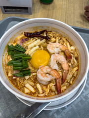 A vibrant bowl of spicy Thai-inspired noodles featuring plump prawns, a rich raw egg yolk, fragrant herbs, and fiery dried chilies. This comforting, flavorful dish offers an authentic taste of