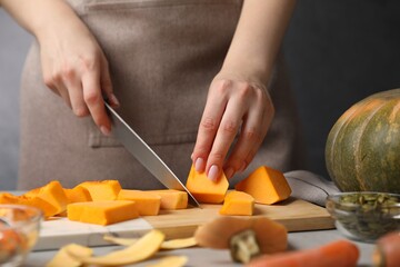 Woman cutting pumpkin at grey table, closeup