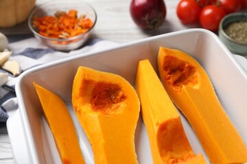 Cut pumpkin in baking dish and ingredients on table, closeup