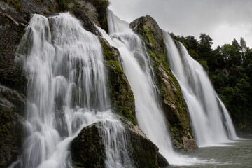 Obraz premium Giant cascading waterfall over green moss covered rocks in New Zealand 