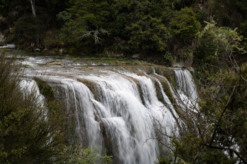 Large cascading waterfall over moss covered rocks in New Zealand nature 