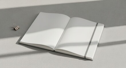 Open white notebook with grey elastic band and binder clip on textured grey surface with light shadows