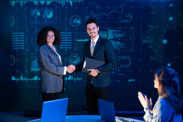 Business professionals finalizing a deal or contract agreement, shaking hands in front of a data analysis screen.