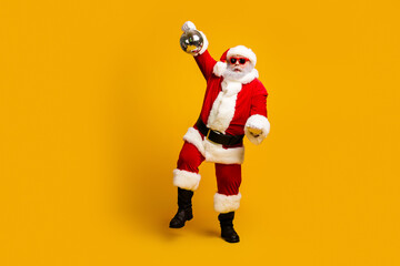 Fun and festive Santa Claus dancing joyfully with a disco ball on a vibrant yellow background wearing red sunglasses