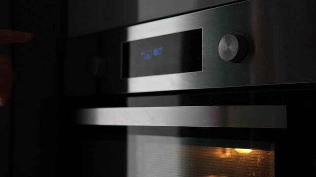 Side view of the woman turning on the electrical oven in the kitchen to baking dessert. Checking readiness of the food