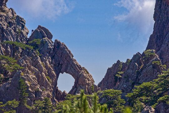 a person climbs onto the bomb hole in the rocks in the Bavella Mountains with sunshine