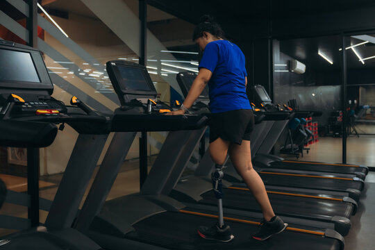 A motivated woman with a prosthetic leg walking on a treadmill in a modern gym, representing fitness, rehabilitation, and strength with a positive attitude towards an active healthy lifestyle.