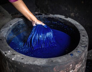 Indigo dyeing: A hand dips a bundle of fabric into a vat of deep blue indigo dye, showcasing the traditional craft.