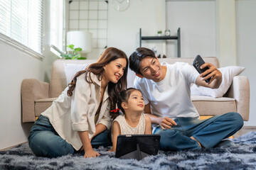Asian family sitting on floor, happy parents and child smiling and bonding while taking a selfie with a mobile phone