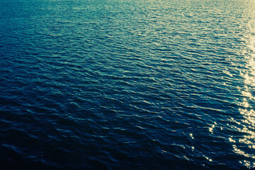 Sea ripples. Bright background. Dark green water. Shallow waves and sun glare on the water. Abstract.