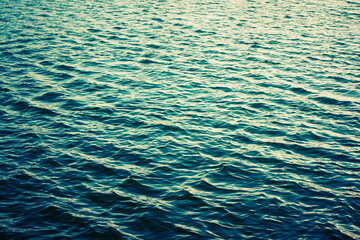 Sea ripples. Bright background. Dark green water. Shallow waves and sun glare on the water. Abstract.