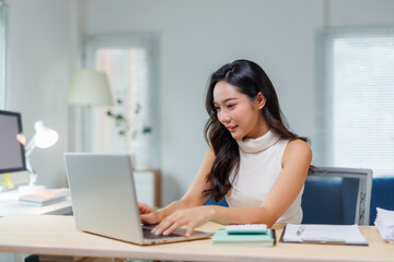 Asian businesswoman typing on computer, managing tasks from home. Remote work concept, happy professional using technology