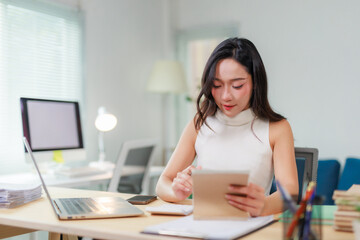 Young Asian woman analyzing financial data and calculating expenses at her modern office desk during work