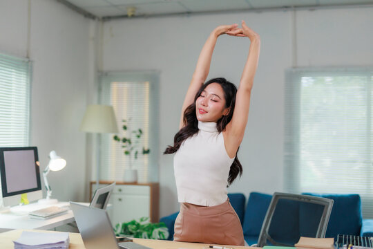 Young woman taking a break from working, stretching arms over her head, finding relaxation and balance in her home office