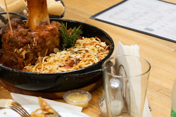 Portion of spaghetti with red sauce and covered in garlic in slices with lamb meat next to the bone in a tray
