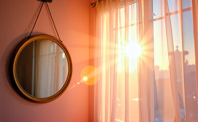 Elegant round mirror reflecting sunlight through sheer curtains in cozy room
