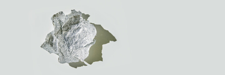 Fototapeta premium Crumpled aluminum foil ball casting shadow on light gray surface.