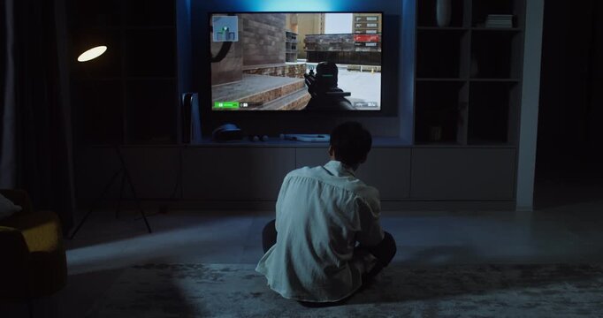 Young man playing video games at home in the evening