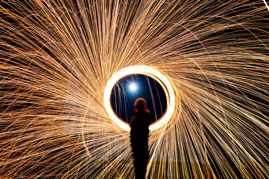 Langzeitbelichtung mit brennender, rotierender Stahlwolle in der Nacht. Funken fliegen kreisf&ouml;rmig und erzeugen dynamische Lichtspuren. 