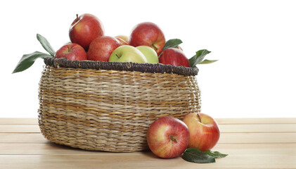Fresh apples in wicker basket and green leaves on wooden table against white background