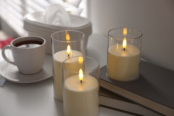 Decorative LED candles, tea, books and tissues on white table indoors, closeup