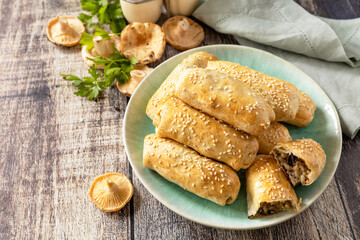 Homemade savory mushroom pastries with sesame seeds on rustic wooden table setting.  Copy space.