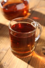 Aromatic black tea in cup and teapot on wooden table, closeup