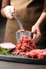 Woman making minced meat with grinder at grey table, closeup