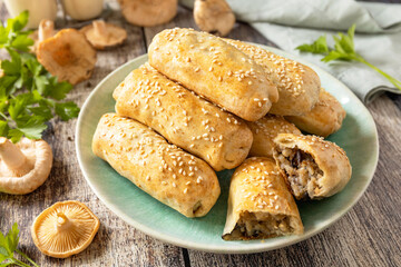 Homemade savory mushroom pastries with sesame seeds on rustic wooden table setting.