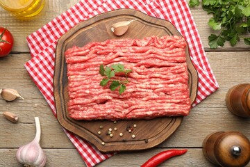 Raw minced meat with parsley and spices on wooden table, flat lay