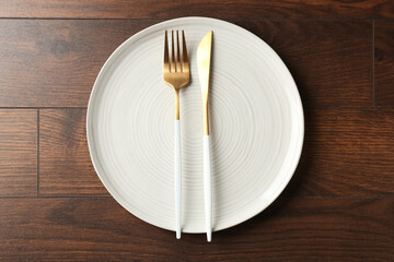 Clean ceramic plate and cutlery on wooden table, top view