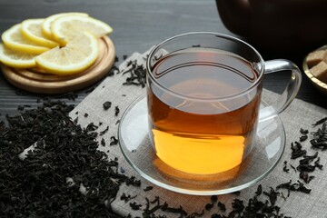 Aromatic black tea in glass cup, dried leaves and lemon on wooden table, closeup