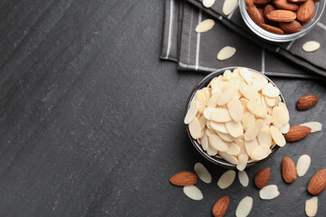 Fresh almond flakes in bowl and whole nuts on grey table, flat lay. Space for text