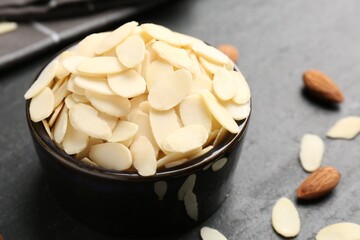 Fresh almond flakes in bowl and whole nuts on grey table, closeup