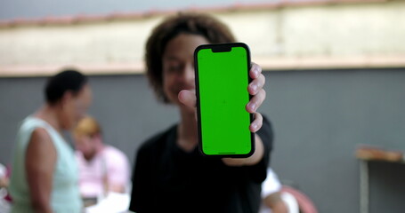 Young boy holding smartphone with green screen chroma key, smiling outdoors in casual courtyard...