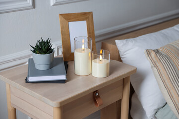 Decorative LED candles, books, floral decor and frame on wooden bedside table indoors