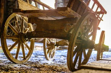 Vintage wooden cart with large wheels resting on a dusty floor in a rustic barn environment during the late afternoon light