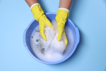 Woman washing clothes in plastic basin on light blue background, top view